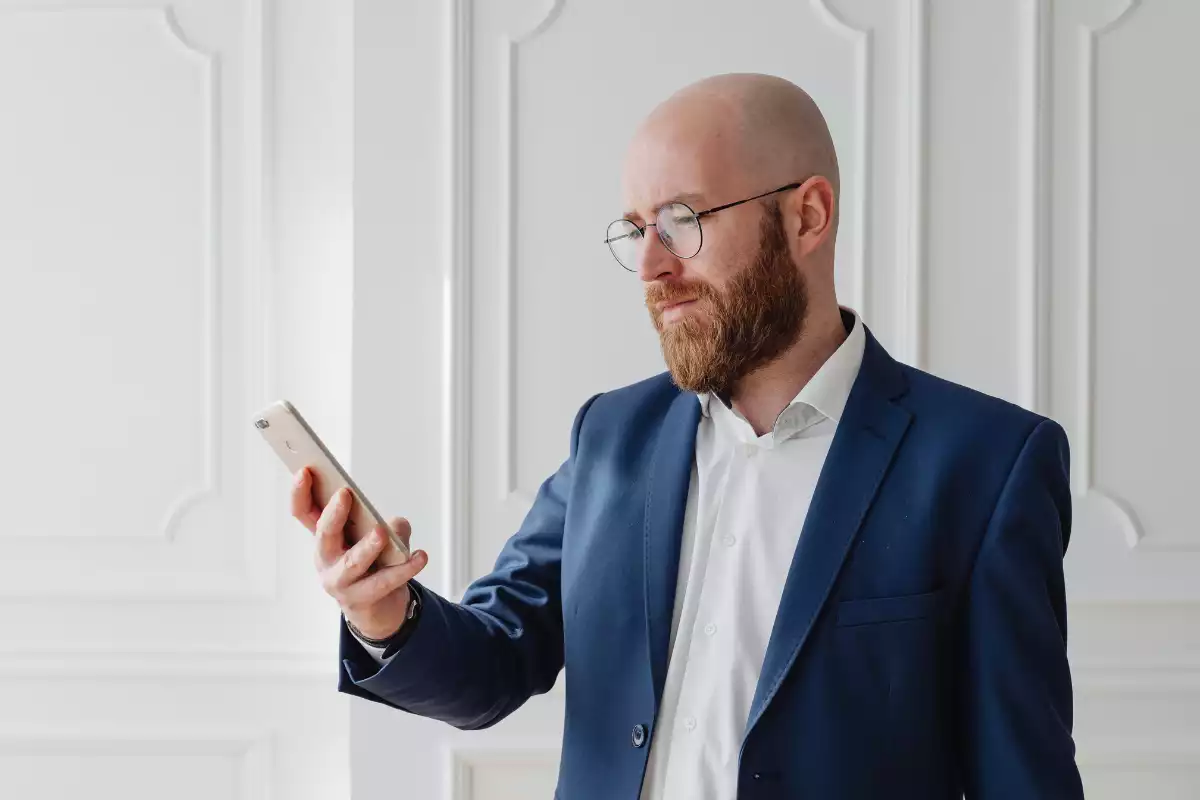 Immagine che raffigura un uomo con gli occhiali e la cravatta mentre guarda lo schermo del suo telefono